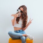 woman in pink tank top and blue denim jeans sitting on yellow chair